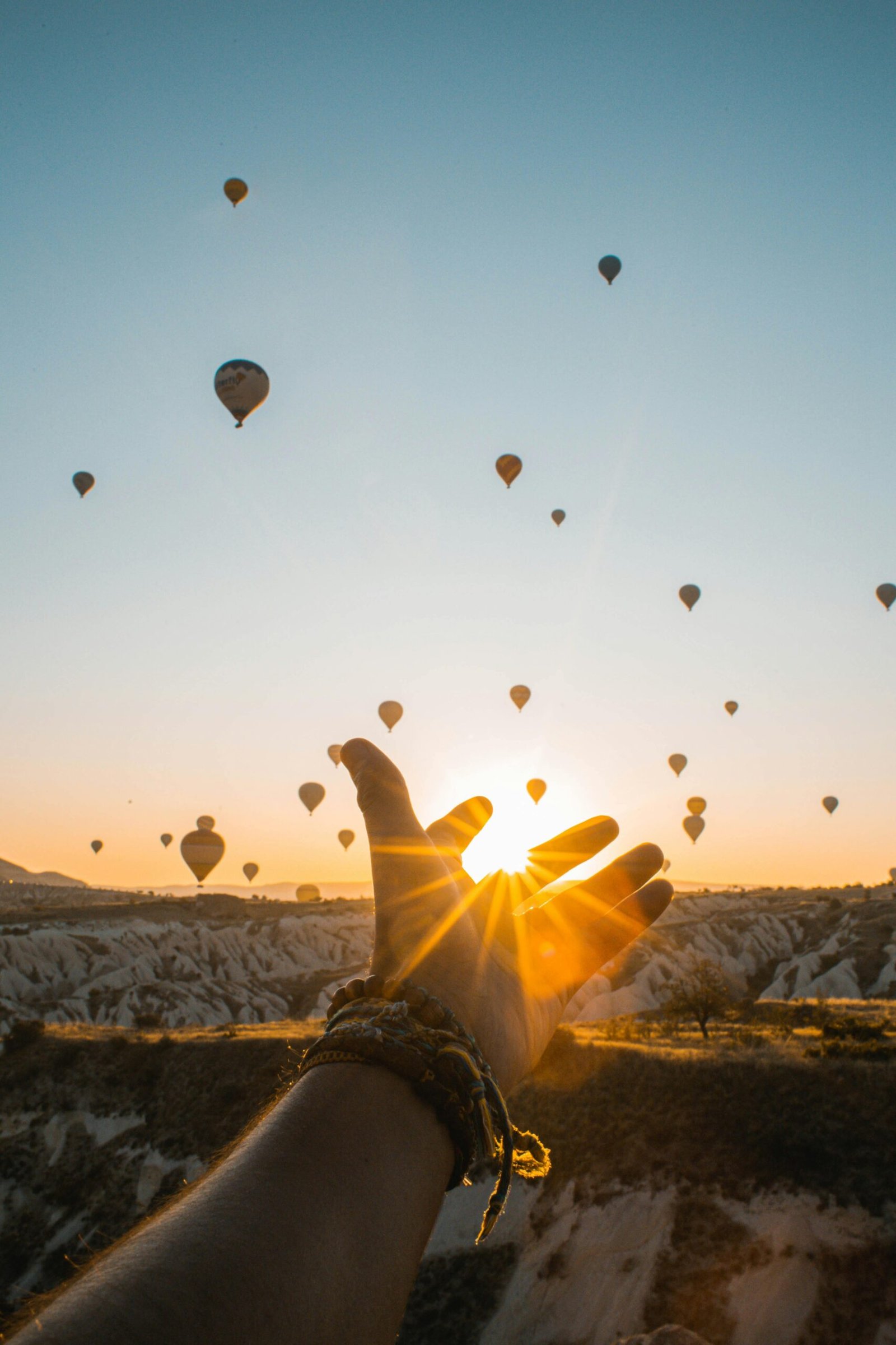 Experience the magic of hot air balloons at sunrise with an outstretched hand in Cappadocia's breathtaking landscape.